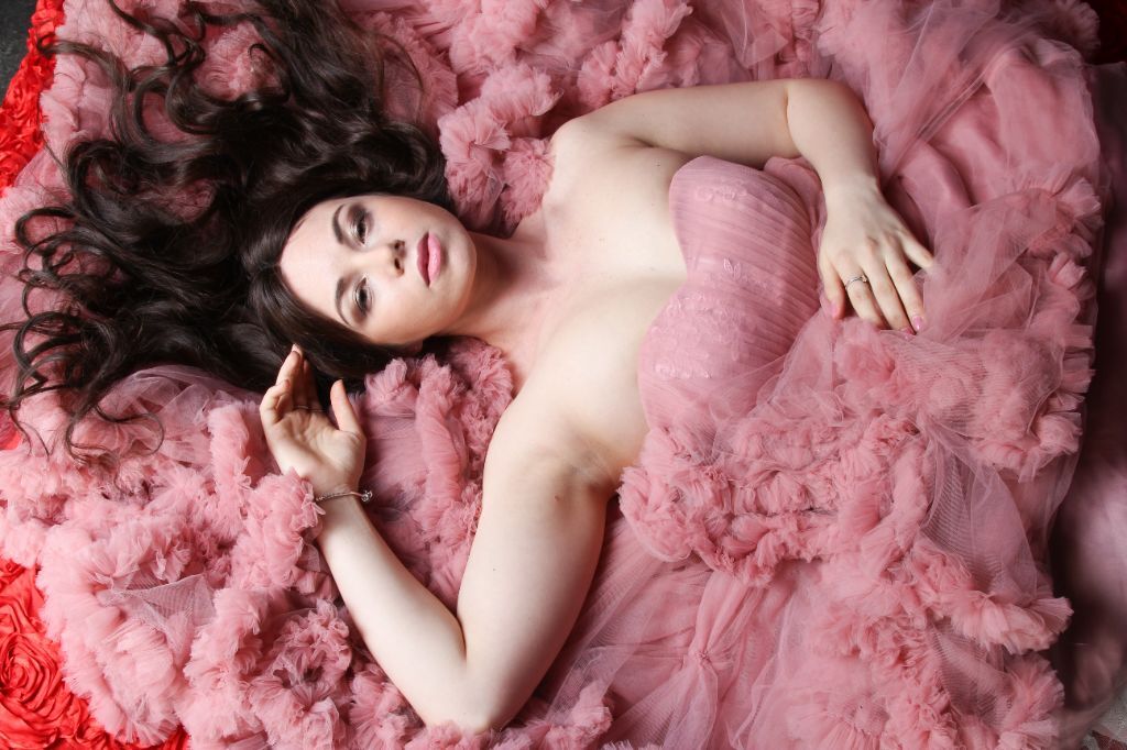 A dreamy homecoming photoshoot, the model lying on the floor, layers of chiffon artfully strewn about her in a formal dress that flatters plus-size bodies.